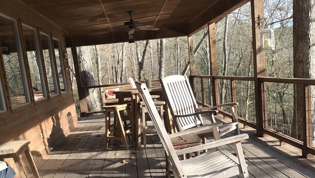 A wooden deck with rocking chairs and a table, surrounded by large windows offering a view of the forest.