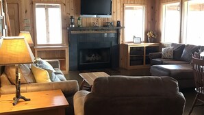 A cozy cabin interior with wooden walls, a fireplace, a television, and comfortable seating.