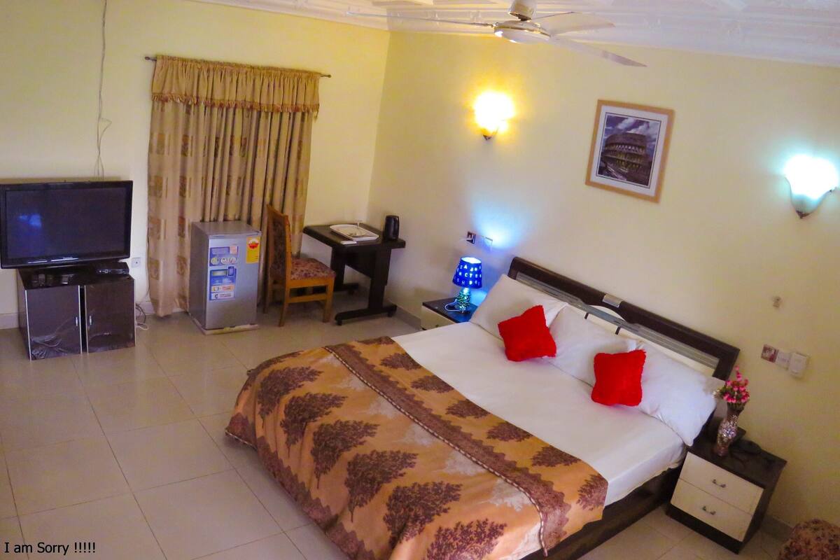 Ein Hotelzimmer mit Bett, Schreibtisch, Fernseher, Minibar und Deckenventilator.