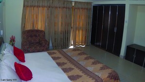 Una habitación de hotel con cama, una silla, armario y aire acondicionado.