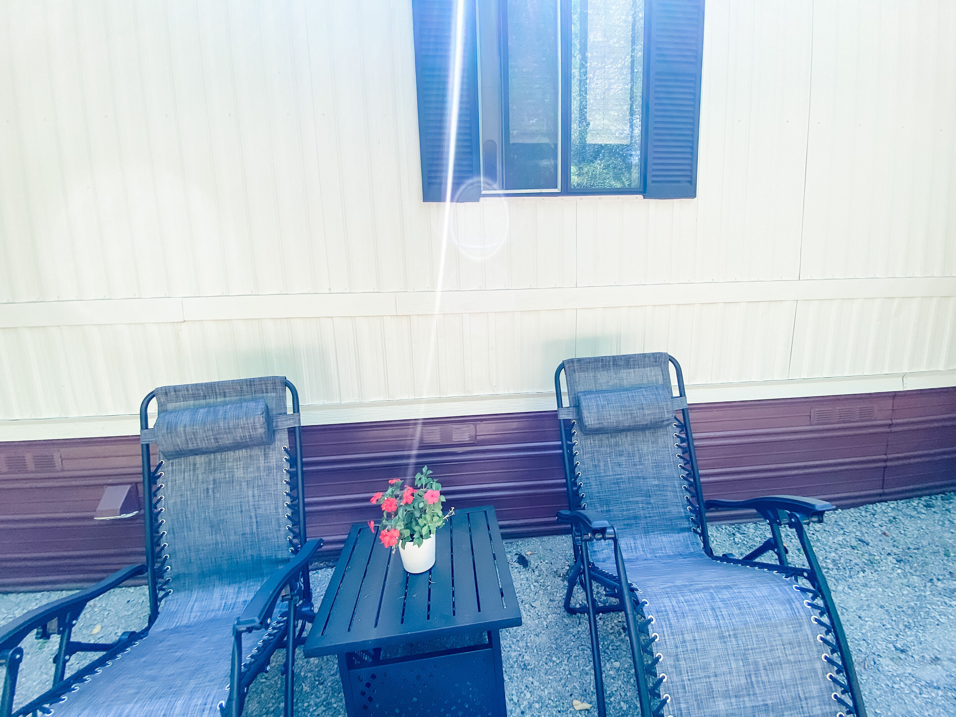 A patio with two chairs and a table, a potted plant, and a window with blinds.