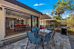 An outdoor patio with a glass table and chairs, a barbecue grill, and a sliding glass door leading to an interior dining area. - Canal-front, Gulf Access Sanctuary kayak and bicycle to the beach (Naples)