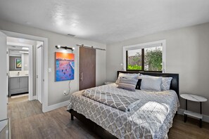Relax in this serene bedroom with a large bed, featuring a patterned bedspread and multiple pillows, and enjoy a view of the surrounding greenery.