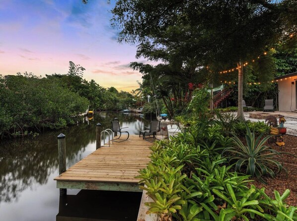 A wooden dock extending into a calm body of water, surrounded by lush greenery and a string of lights. - Canal-front, Gulf Access Sanctuary kayak and bicycle to the beach (Naples)