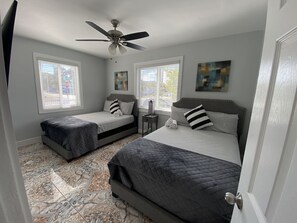 A bedroom with two beds, a ceiling fan, and a window with blinds.