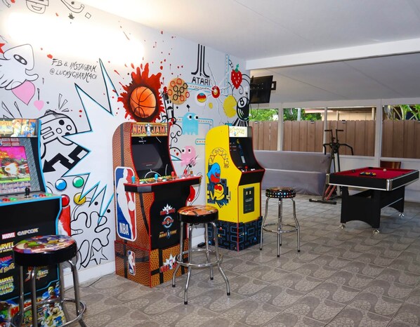A room with arcade games, a pool table, and a mural with various sports and entertainment themes.
