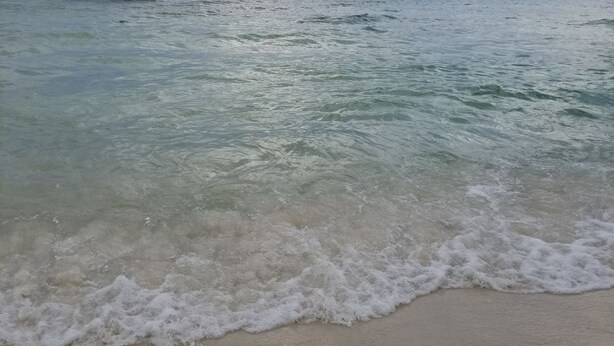 Ein Strand mit klarem Wasser und sanft brandenden Wellen.