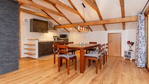 A spacious loft with exposed wooden beams, a kitchen with modern appliances, and a dining area with wooden furniture. - Apartment Panorama (Reit im Winkl)