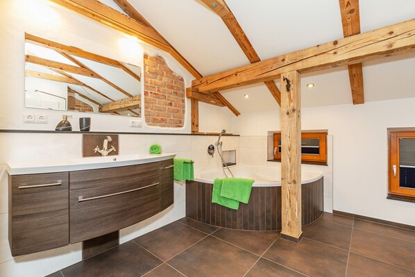 A modern bathroom with a bathtub, a vanity with drawers, a mirror, and wooden beams on the ceiling. - Apartment Panorama (Reit im Winkl)