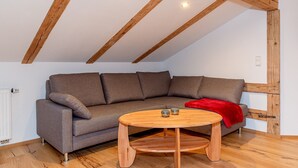 A loft-style room with a wooden ceiling, a gray sectional sofa, a wooden coffee table, and a red throw blanket. - Apartment Panorama (Reit im Winkl)