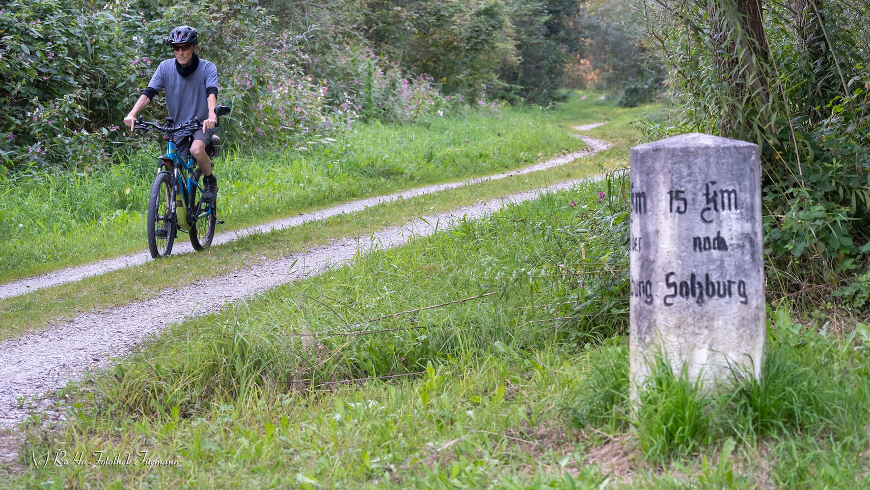 Ciclista en un camino de grava con un cartel que indica una distancia de 15 km hasta Solzberg.