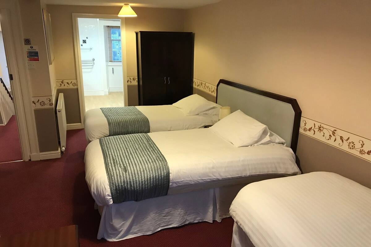 A hotel room with two beds, a wardrobe, and a door leading to a corridor.