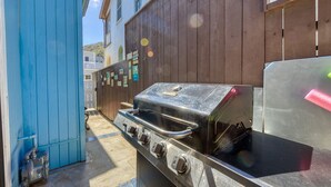Un espace barbecue extérieur avec une porte bleue, une clôture en bois et un ciel dégagé.