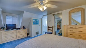 Une chambre à coucher comprenant un lit, un ventilateur de plafond, une commode, un téléviseur et une porte donnant sur une autre pièce.