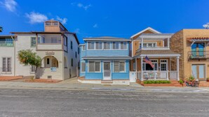 Une rangée de bâtiments à trois étages, avec une maison bleue au centre, une maison beige dotée d’un balcon et une maison brune avec un porche.