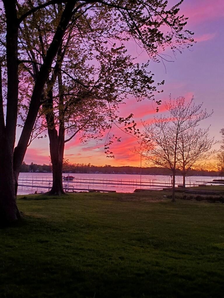 Un parc avec des arbres et une étendue d’eau, au coucher du soleil.