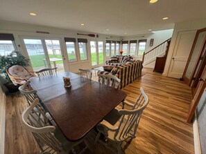 Enjoy meals in this dining area with a long table and comfortable seating, offering a view of the outdoors and a staircase to the upper level.