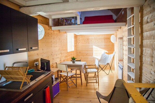Une cuisine compacte aux murs en bois, un coin repas avec une table et des chaises, et une petite fenêtre qui laisse entrer la lumière naturelle.
