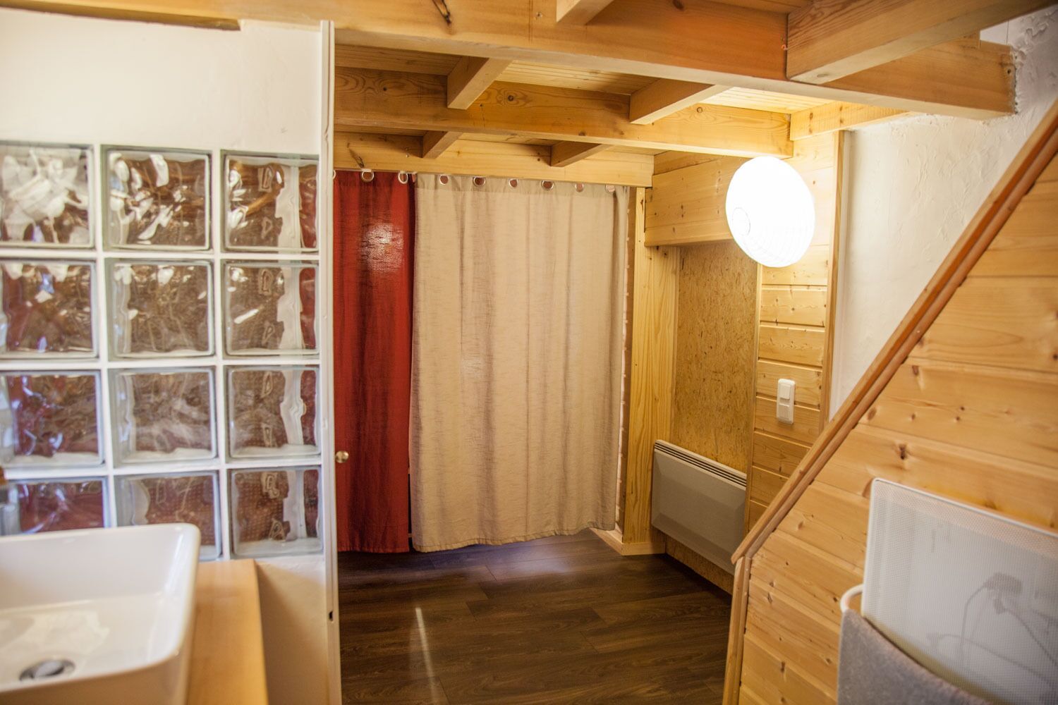 Un interior de madera con una escalera de madera, un radiador y una ventana con cortinas.