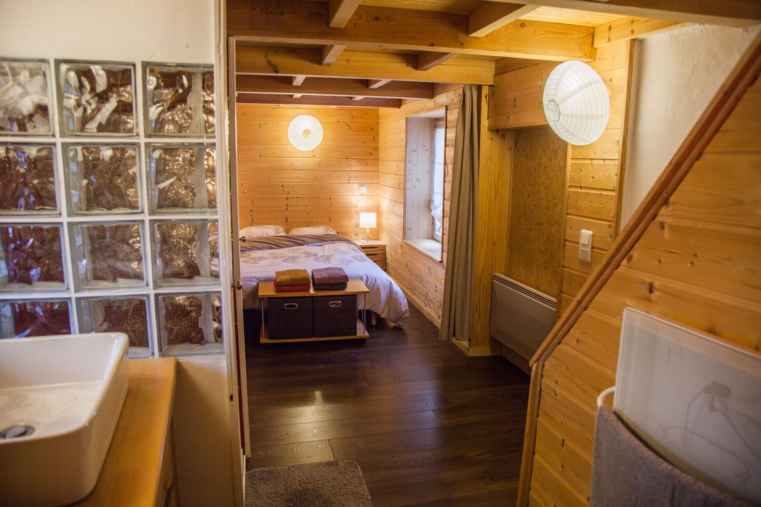Un intérieur en bois comprenant un lit, une table de chevet, un radiateur et une fenêtre avec des rideaux.