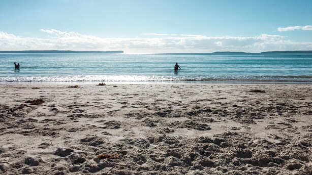 A beach with two people in the water, a clear sky, and distant land. - The Heart of Huskisson (Huskisson)