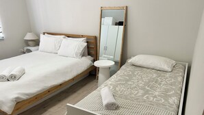 Two single beds with white linens, a small round table, a mirror, and a wooden wardrobe. - The Heart of Huskisson (Huskisson)