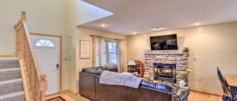 A living room with a stone fireplace, a sofa, a dining table, and a staircase.