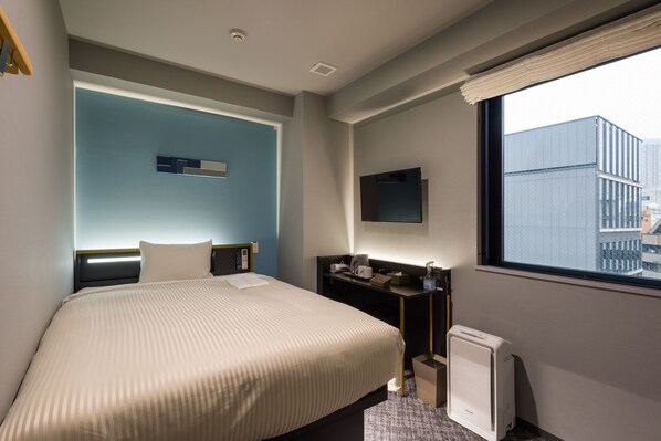 Een hotelkamer met een groot bed, een bureau met stoel, een aan de muur bevestigde televisie en een raam met uitzicht op de stad.