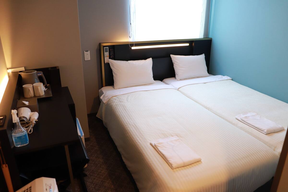 Une chambre d’hôtel avec deux lits, un bureau avec un téléphone et une machine à café, ainsi qu’une fenêtre avec des stores.