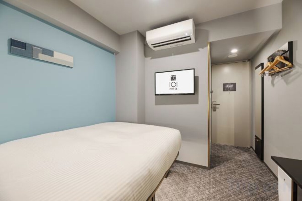 Ein Hotelzimmer mit einem Bett, einer Klimaanlage, einem Fernseher und einer Tür zu einem anderen Raum.