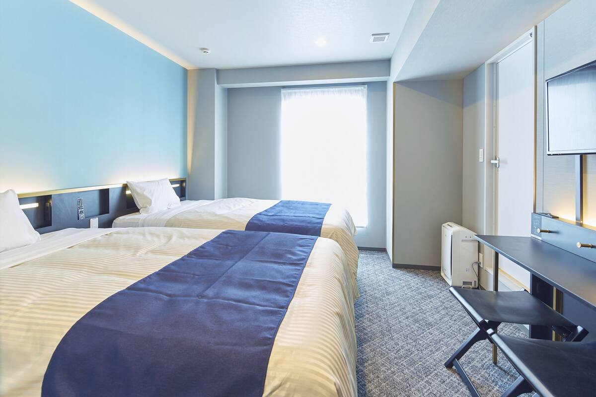 Une chambre d’hôtel avec deux lits, un bureau et une grande fenêtre.
