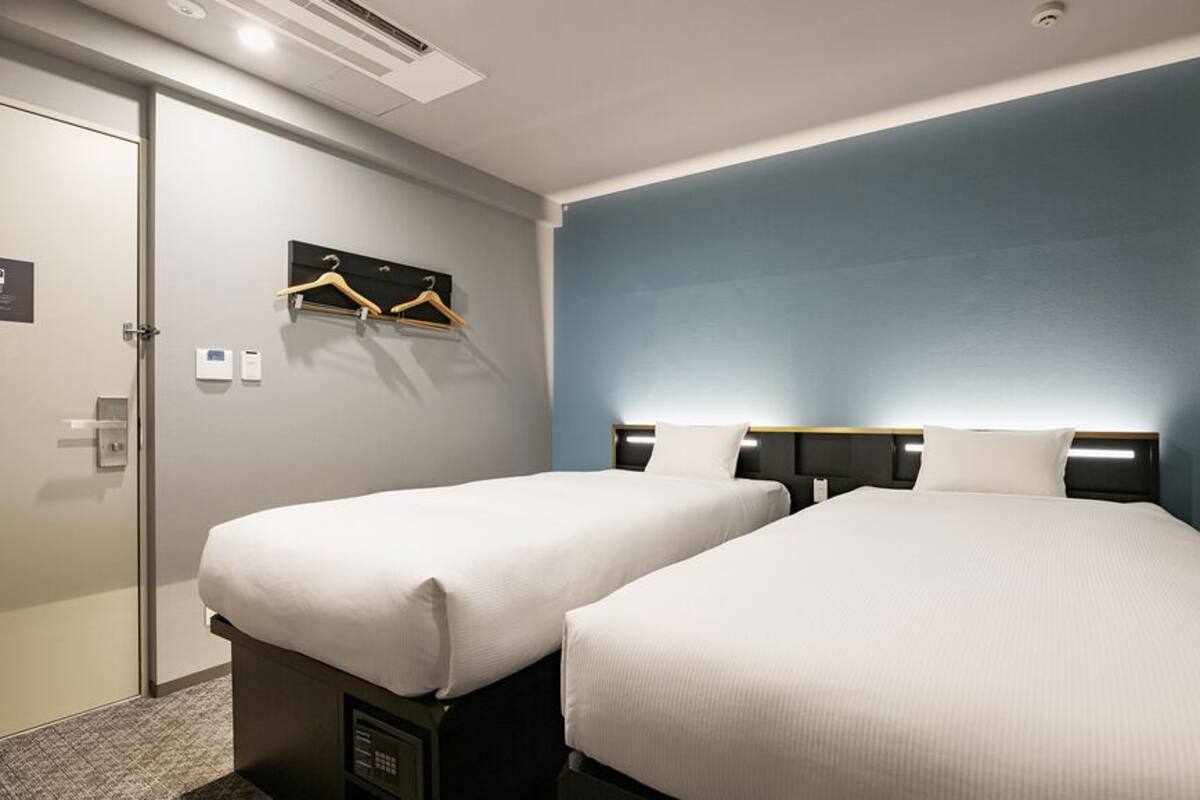 A hotel room with two beds, a wall-mounted TV, a coat rack, and a door with a handle.