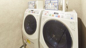 Deux machines à laver à chargement frontal se trouvent dans une buanderie, avec leurs panneaux de commande et leurs consignes de sécurité.