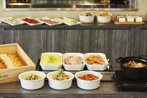 Een buffet met diverse gerechten, waaronder brood, salades, pasta en warme maaltijden.