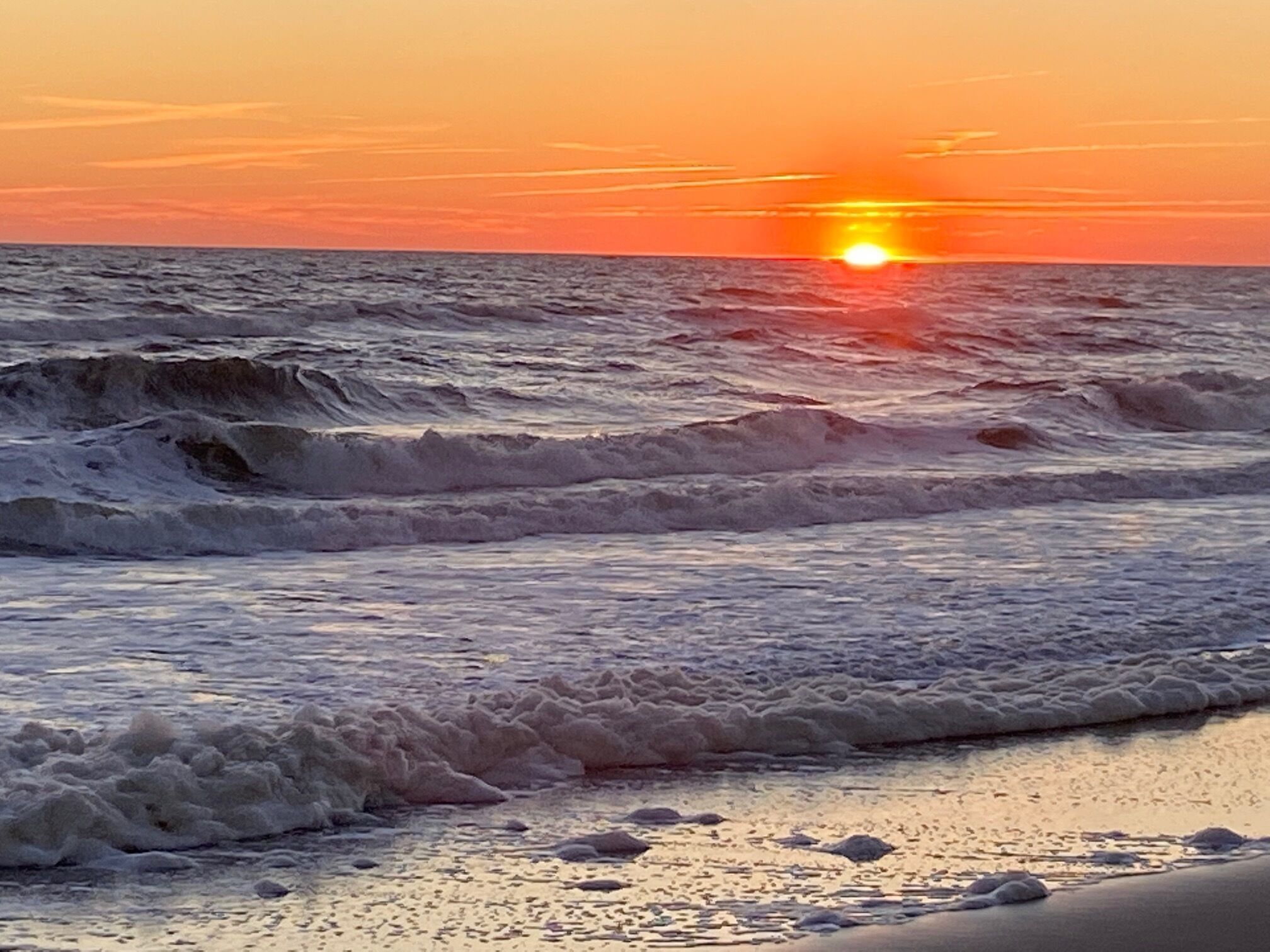 A beach with waves and a sunset.