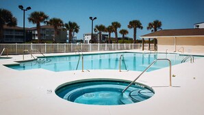 A swimming pool with a hot tub, surrounded by palm trees and a white fence. - Spacious clean condo,  large pool, plus many extras.   Perfect for families. (Oak Island)