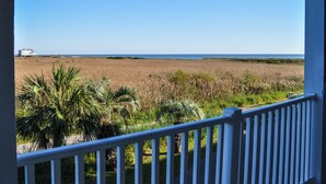 A balcony with a view of a beach and a distant house. - Spacious clean condo,  large pool, plus many extras.   Perfect for families. (Oak Island)