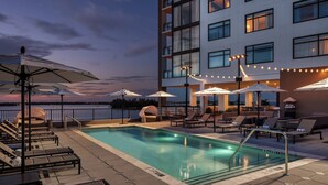 A rooftop pool area with lounge chairs and umbrellas, a pool, and a building with multiple floors and balconies. - Luminary Hotel & Co., Autograph Collection (Fort Myers)