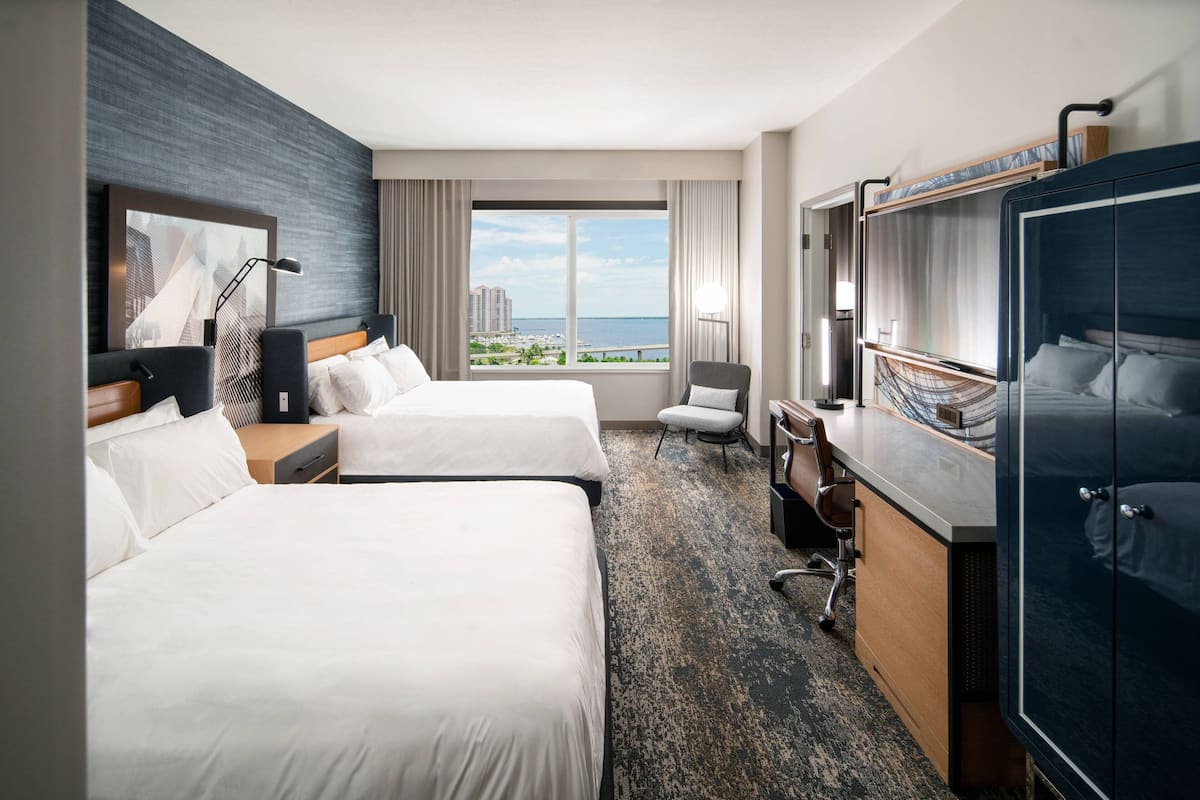 A hotel room with two beds, a desk, a chair, and a large wardrobe.