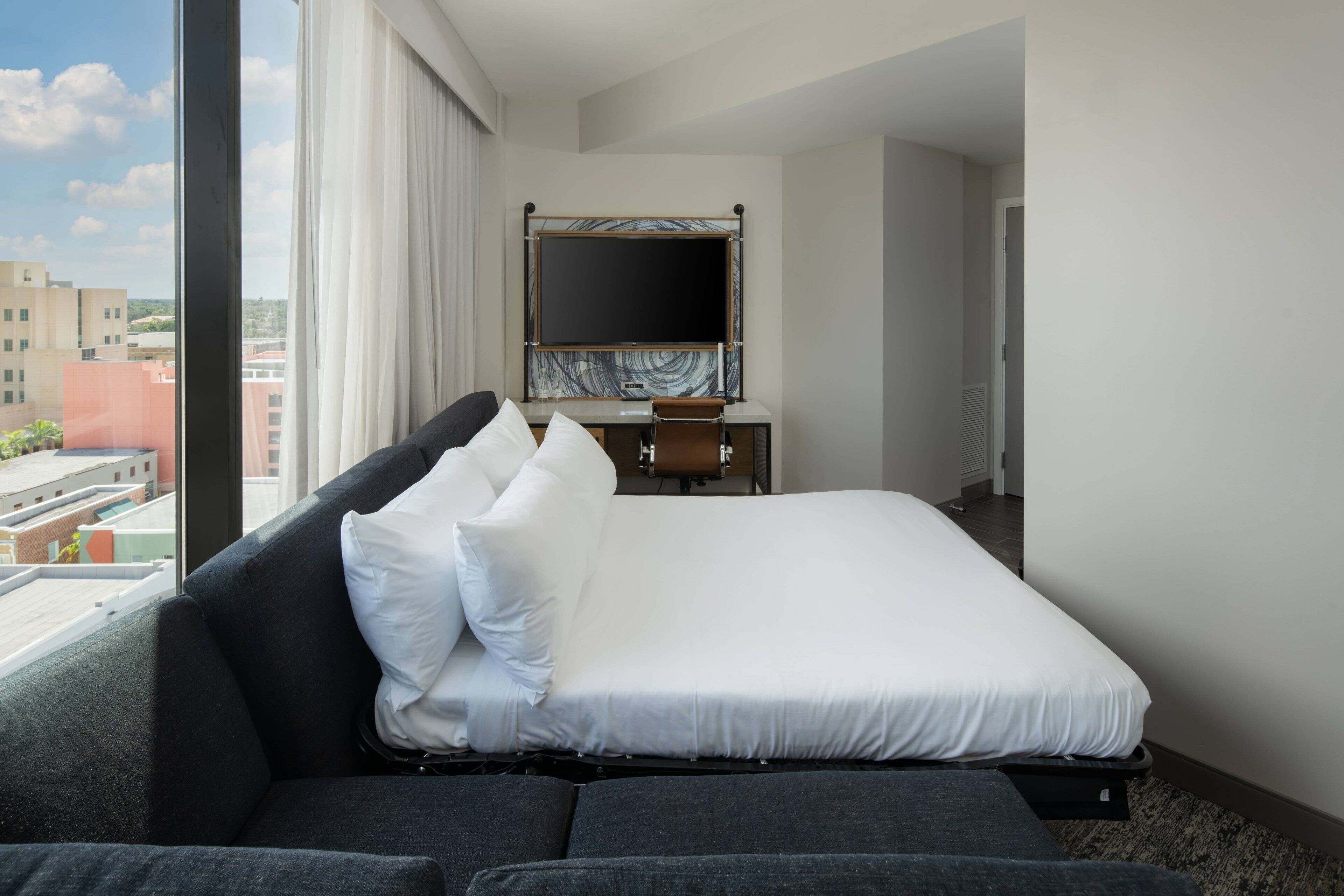 Habitación de hotel con cama, escritorio y ventana grande que ofrece vistas a la ciudad.
