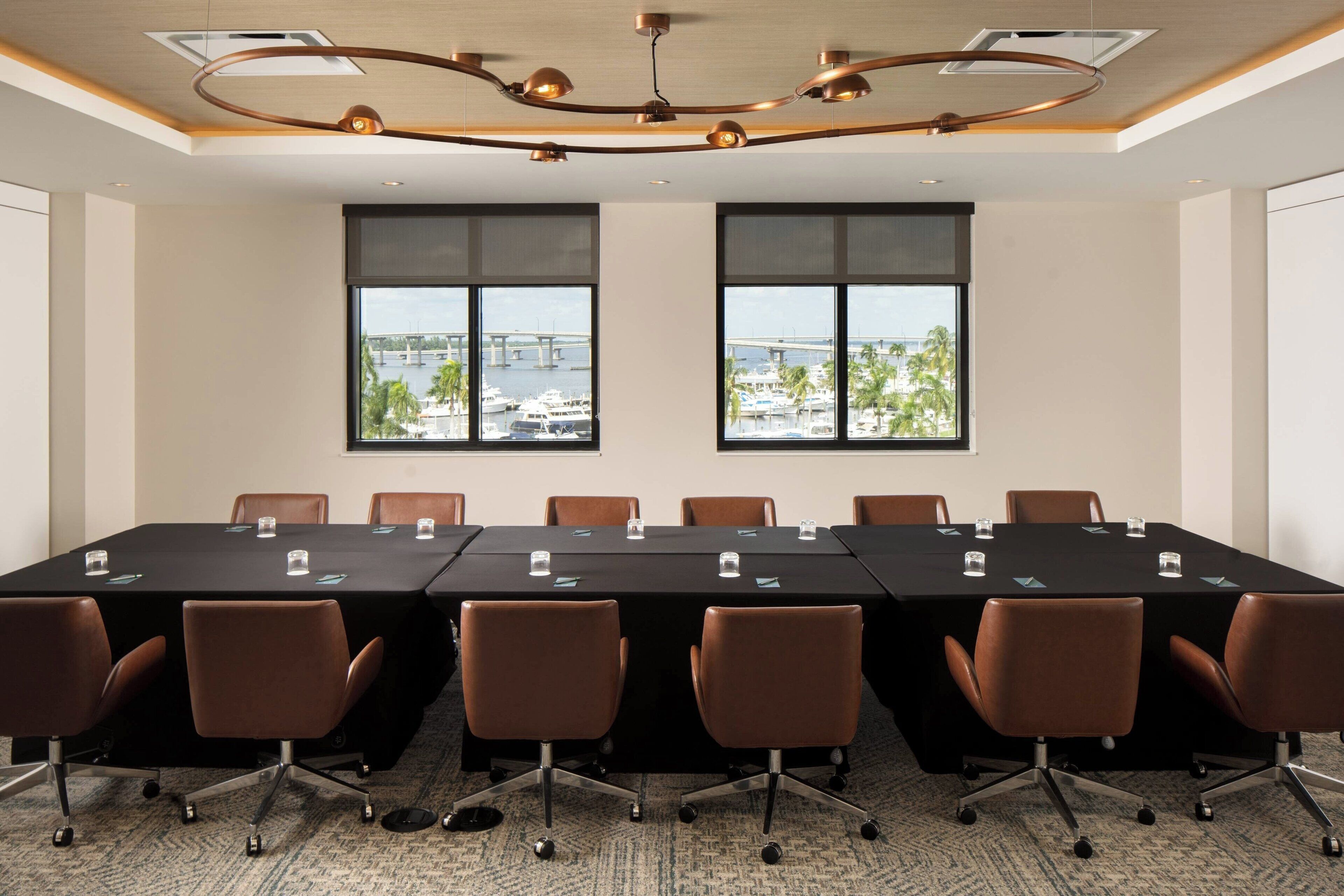 Une salle de conférence dotée d’une longue table, de chaises marron et de grandes fenêtres offrant une vue sur des bateaux et un pont.