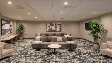 A hotel lobby with a patterned carpet, a sofa with multiple cushions, a coffee table, and two potted plants.
