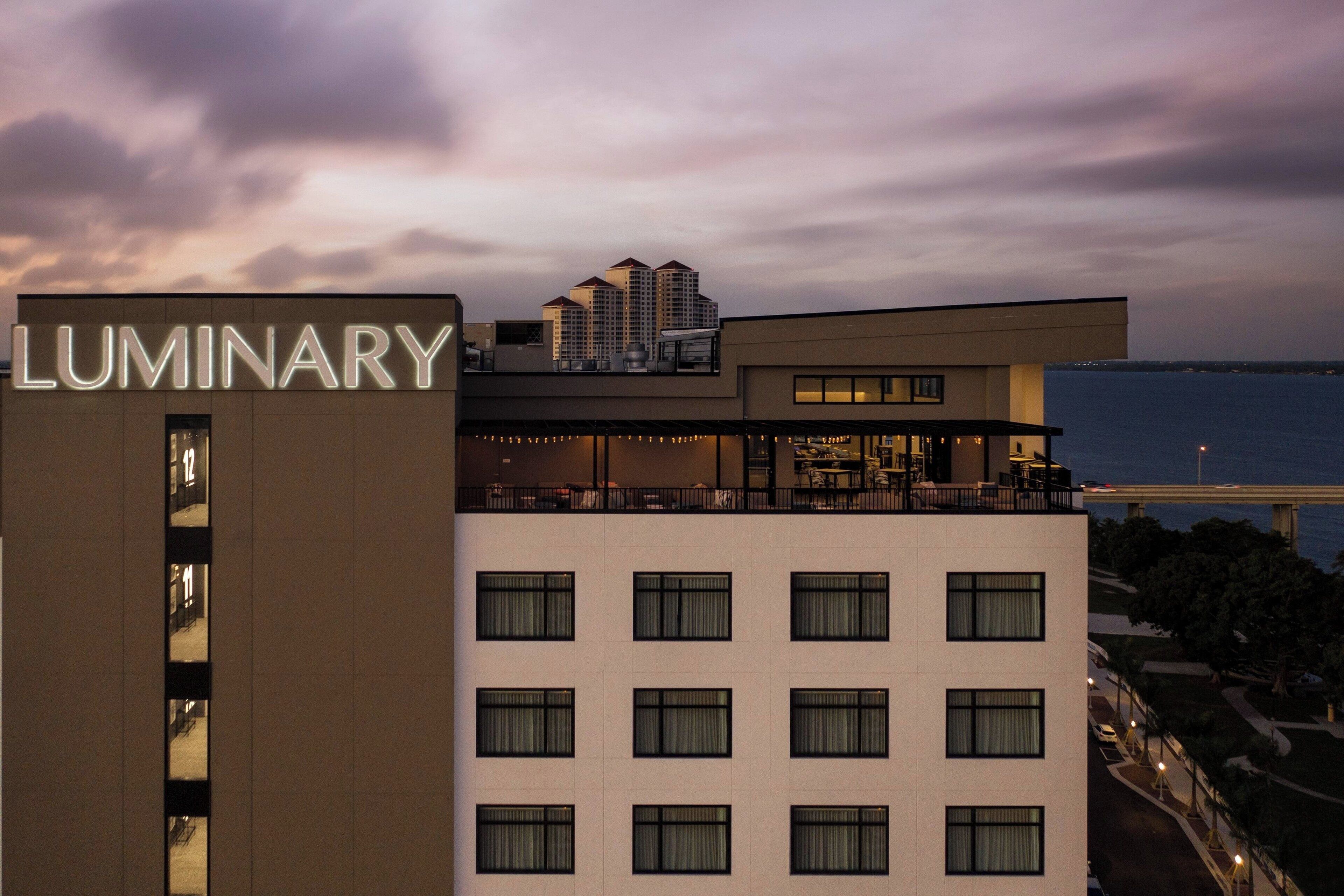 A hotel with a modern design, featuring a prominent 'LUMINARY' sign, multiple floors, and a view of the sea.