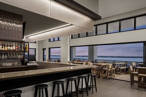 Een moderne barruimte met een lange toonbank, krukken en uitzicht op het water.
