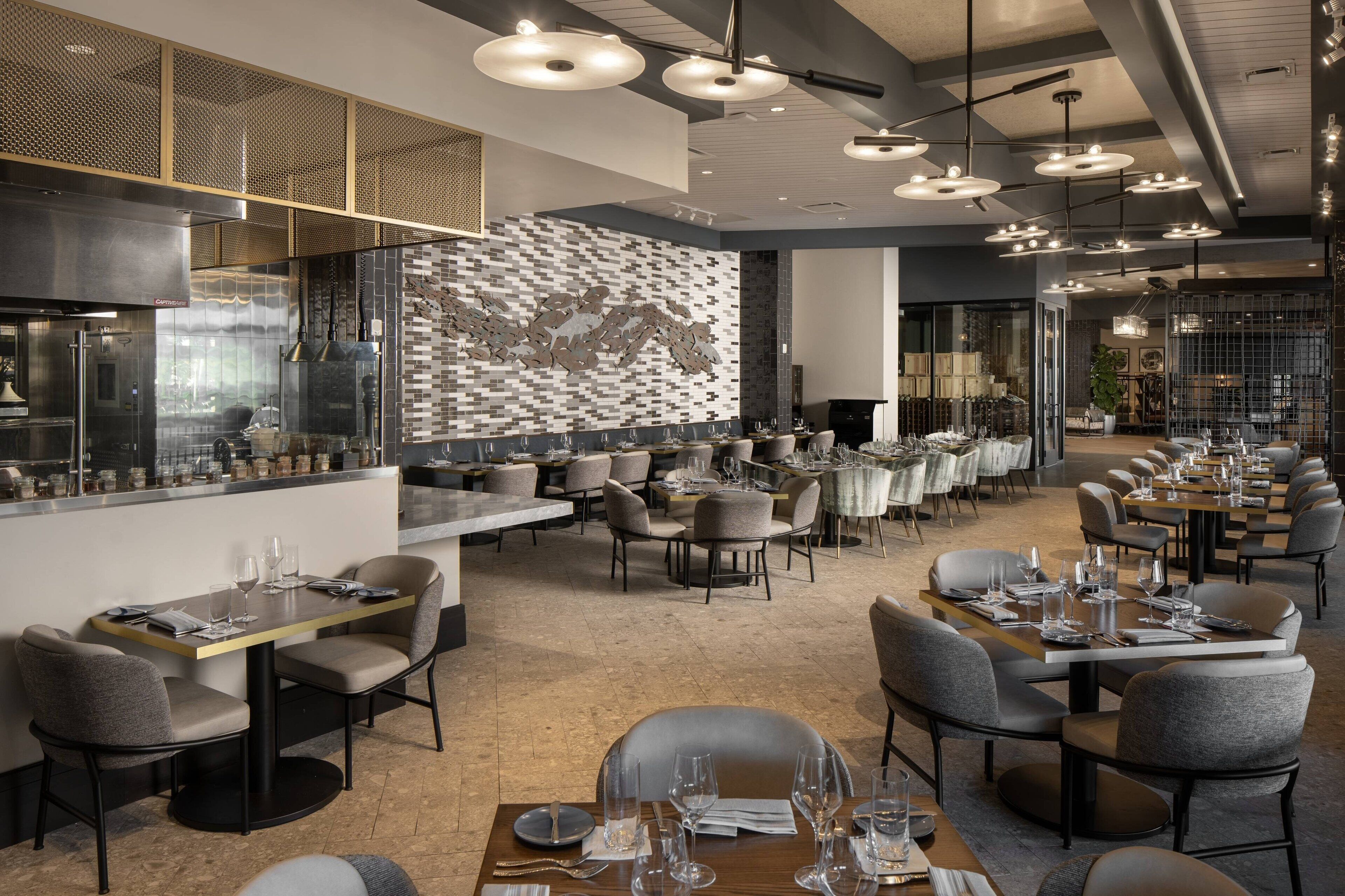 Un restaurante moderno con un amplio comedor, varias mesas y luminarias contemporáneas.