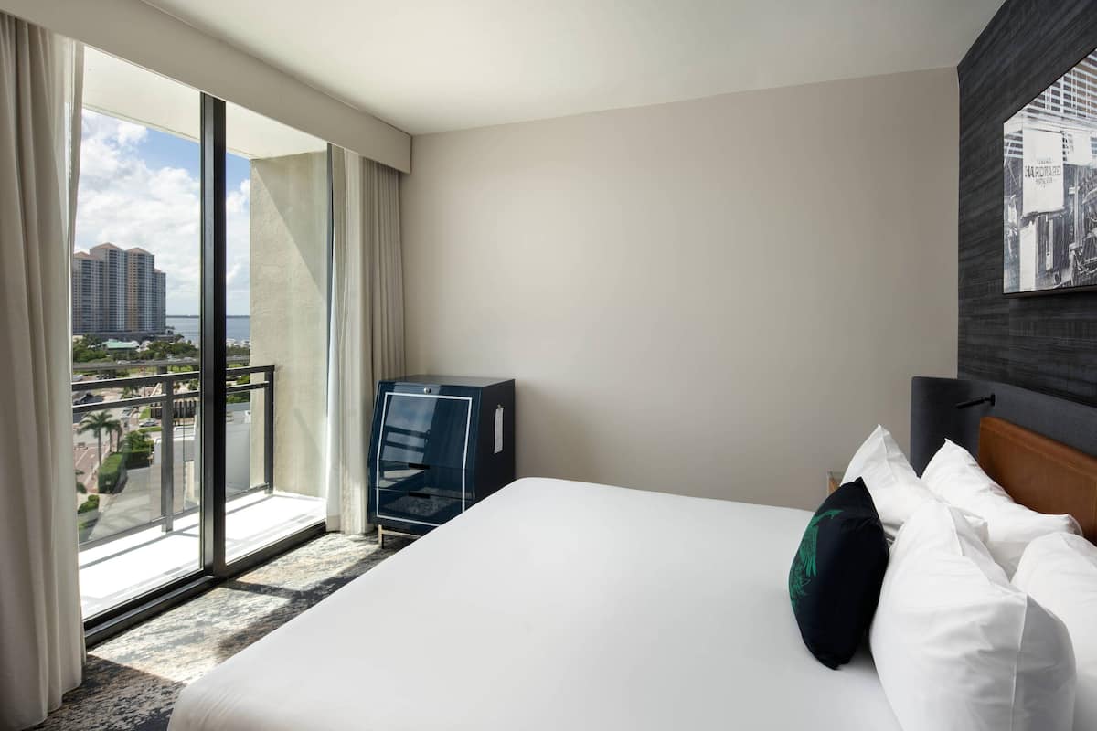 Habitación de hotel con una cama grande, vista de la ciudad desde un balcón y un cabecero oscuro.