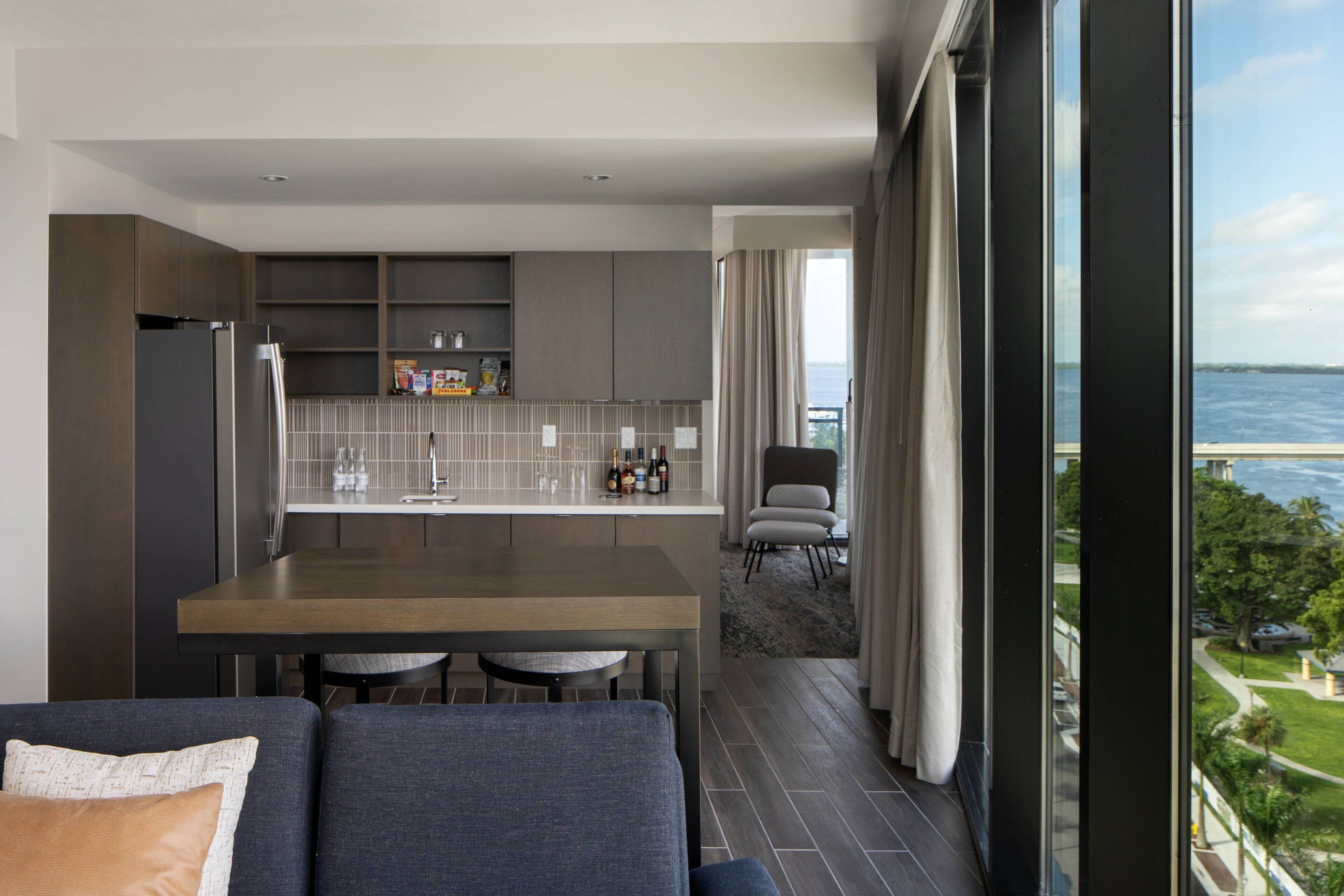 A modern kitchen with a dining area, large windows, and a view of the sea.