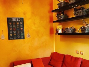 Quarto com parede amarela, sofá vermelho e estantes com cestos e chaleira.