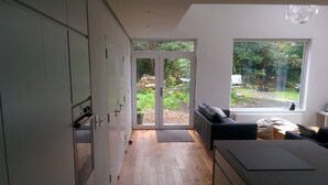 A modern kitchen with wooden flooring, a built-in oven, and a sliding glass door leading to a garden. - Exclusive Garden Apartment (Galway)