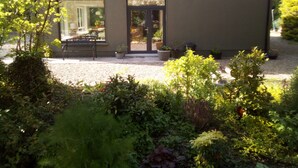A modern building with a gravel driveway, a bench, and various potted plants. - Exclusive Garden Apartment (Galway)